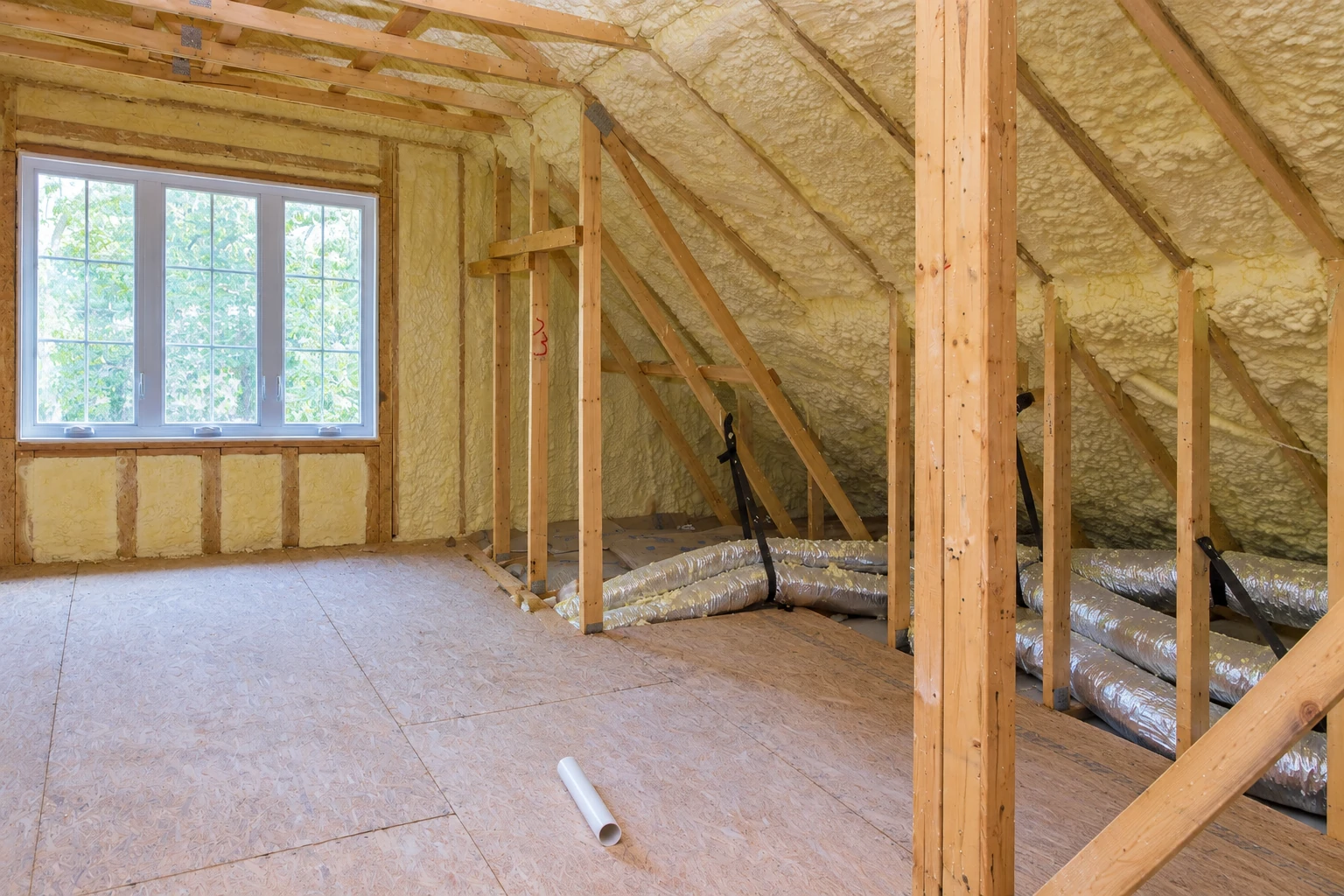Attic rafters and walls covered with spray foam insulation, with exposed framing and flexible ducts on the floor.