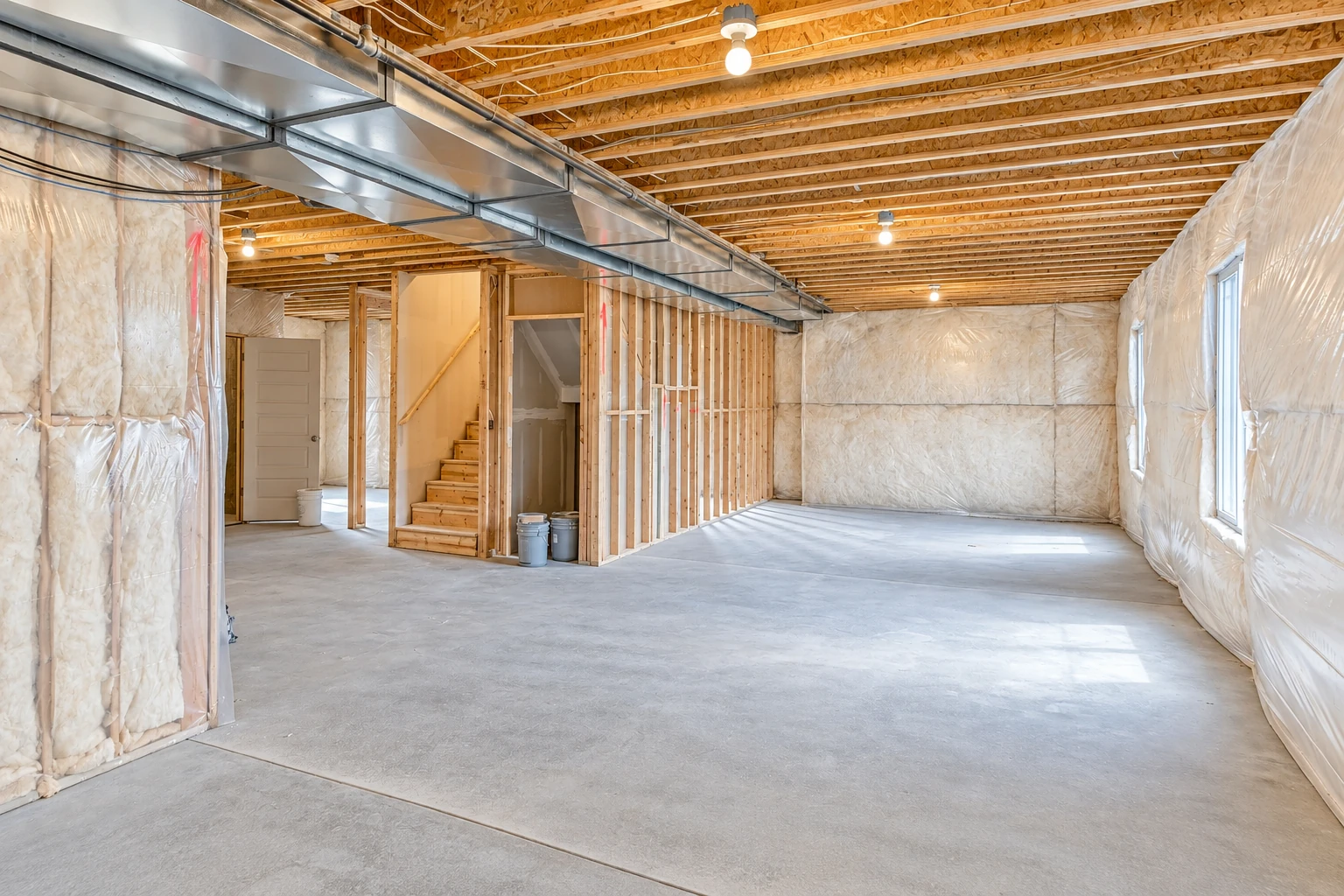Basement with insulated walls, exposed ceiling joists, a metal air duct, and an open concrete floor.
