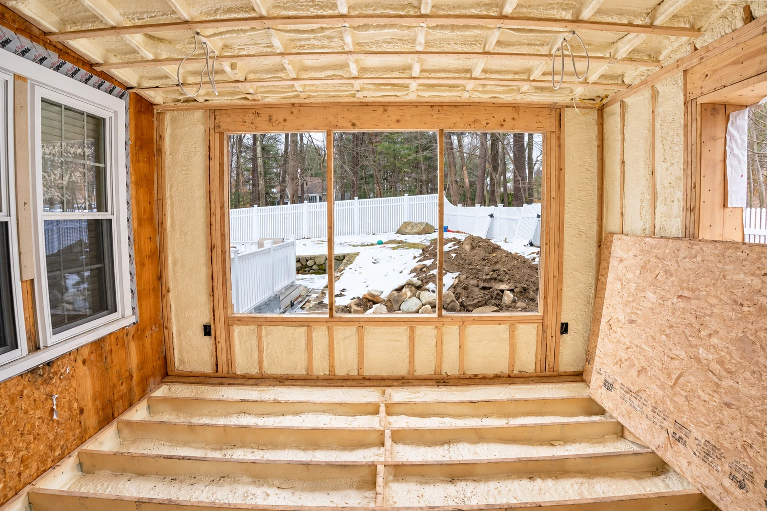 A room under renovation with pale spray foam covering the walls, ceiling and floor joists.