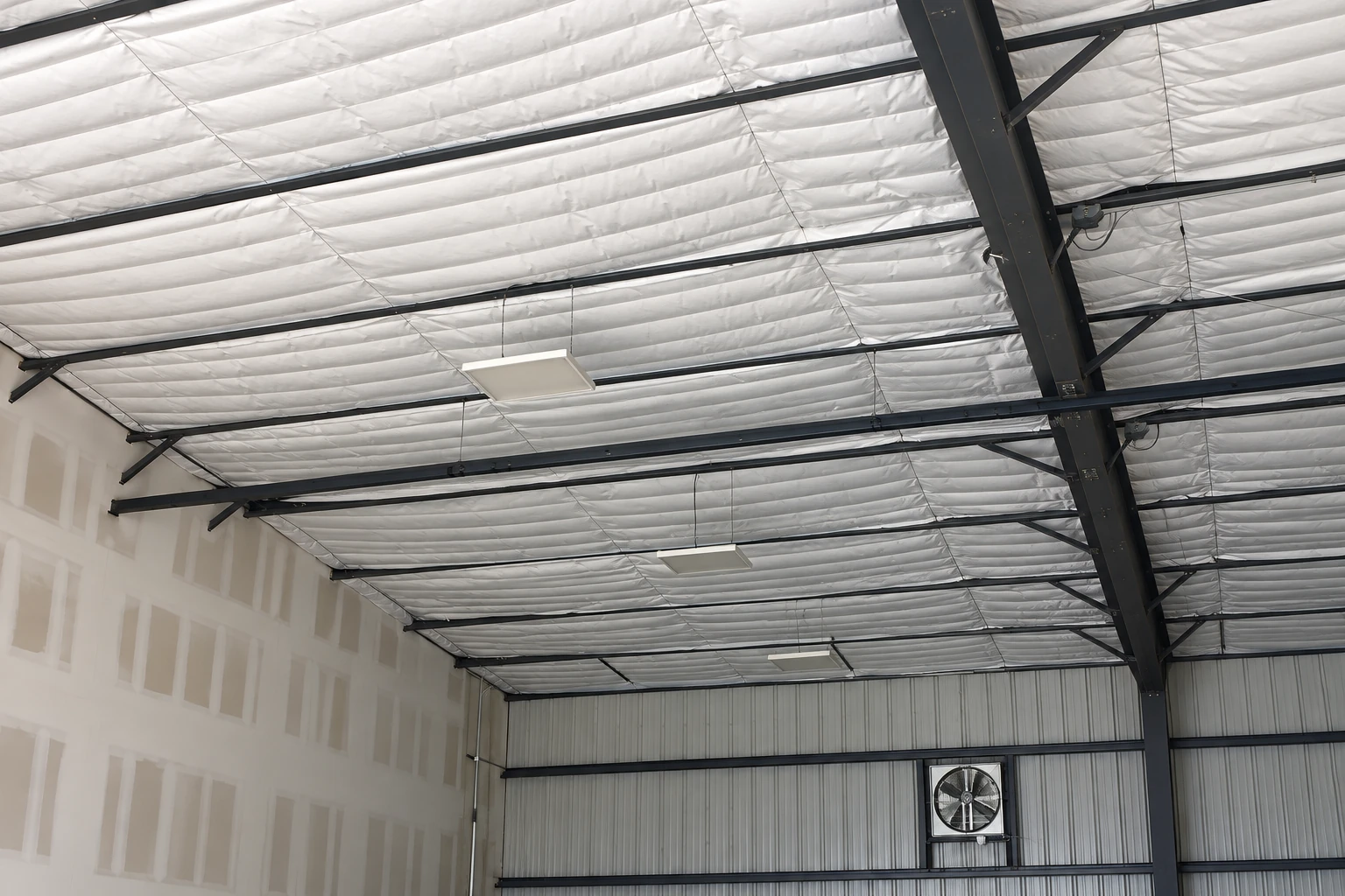 Reflective white insulation lines the ceiling of a large metal-framed building.
