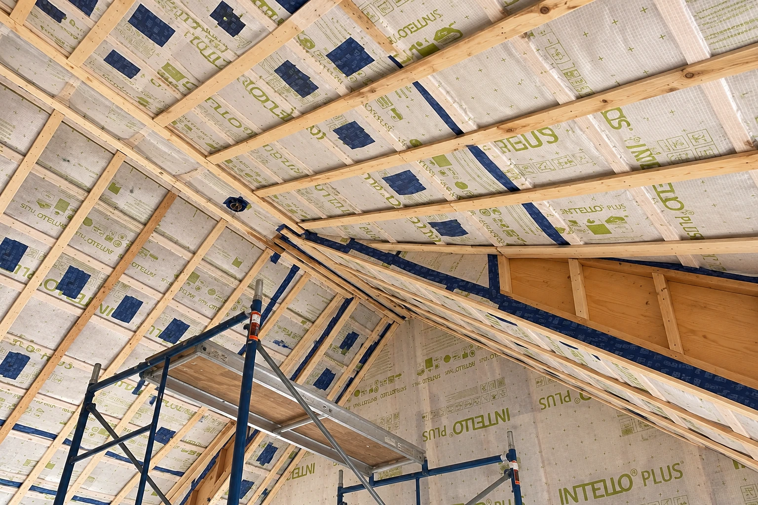 Printed vapor barrier membrane is being installed across the rafters and walls of a wood-framed attic.