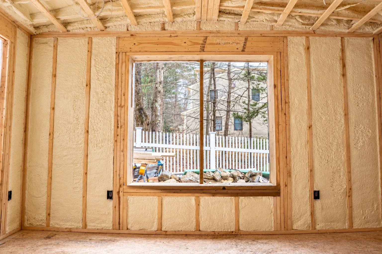 Unfinished room with spray foam insulation between wall studs around a large central window.